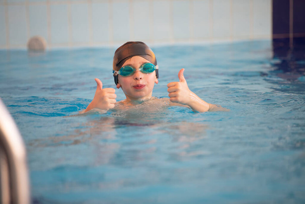Niño con gorra de baño y gafas de baño en la piscina. El niño se dedica a la sección de natación. - Foto, Imagen