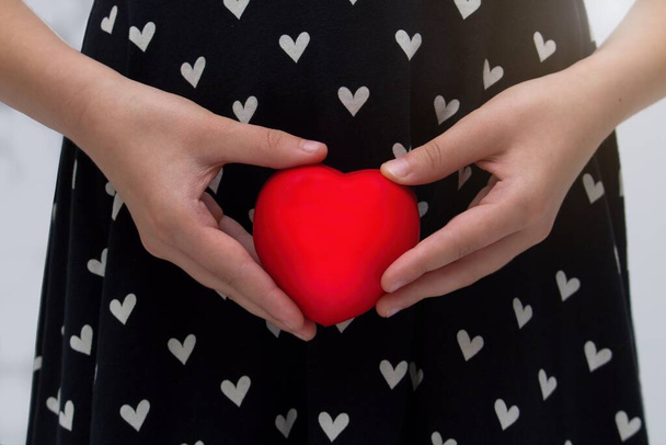 Dziewczyna lub kobieta ubrana w sukienkę z sercami trzymającymi czerwone serce przed jej klina. Koncepcja zwrócenia uwagi na problemy ginekologiczne kobiet i konieczność zapobiegania. - Zdjęcie, obraz