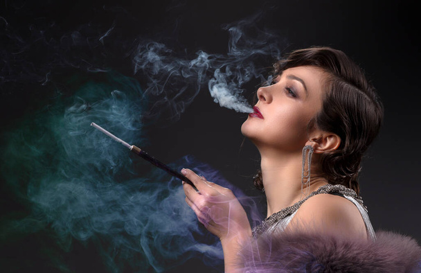 Портрет ретро-жінки. Красива жінка в стилі 20-х або 30-х з мундштуком в кольоровому димі
. - Фото, зображення