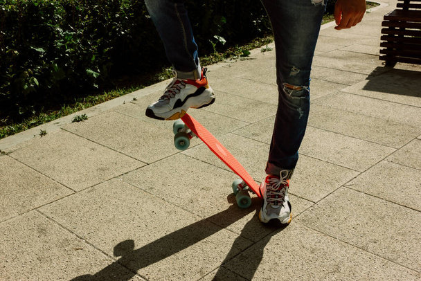 Young guy in ripped jeans standing with penny board in the park. summer activities skateboarding - 写真・画像