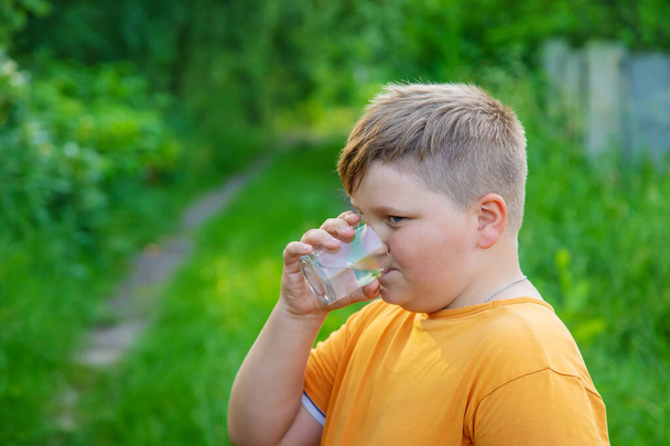 A kisfiú pohárból issza a vizet. Szelektív fókusz. Kölyök!. - Fotó, kép