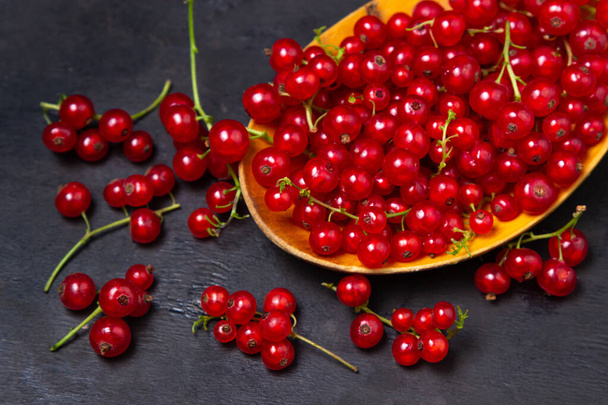 Red currants in a wooden spoon on a black background. Lots of ripe red currants. Delicious berry. - Foto, immagini