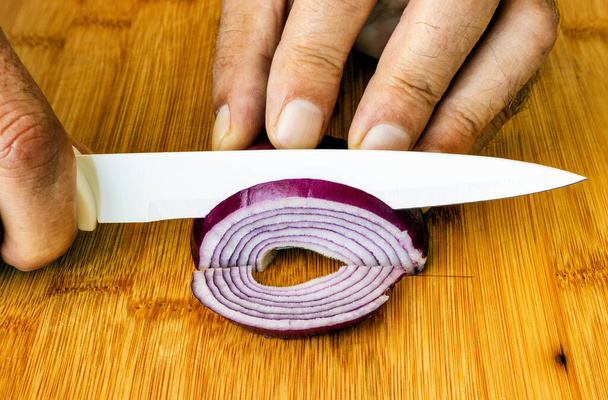 un homme avec un couteau en céramique sur une planche à découper coupe un oignon - Photo, image