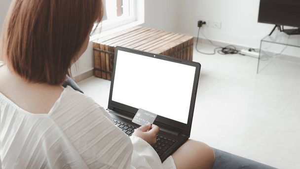 Nainen, jolla on luottokortti, joka maksaa verkossa, kannettavalla tietokoneella, istuu olohuoneen sohvalla, kotona leikkauspolulla. Käsite online shopping.white screen kannettavan mockup - Valokuva, kuva