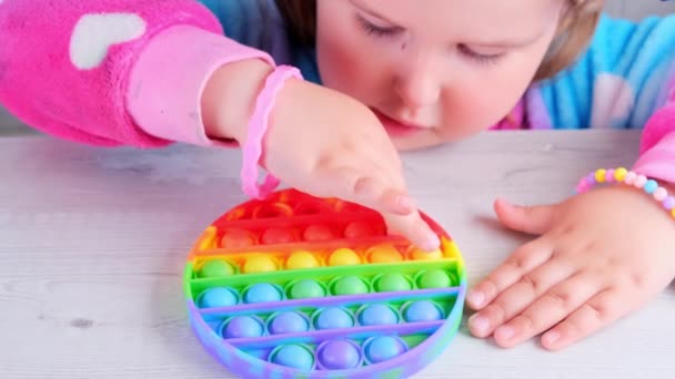 cute little girls playing with enthusiasm pop it sensory toy circle form. little female presses colorful rainbow squishy soft silicone bubbles on white background. Stress and anxiety relief. Trendy - Footage, Video