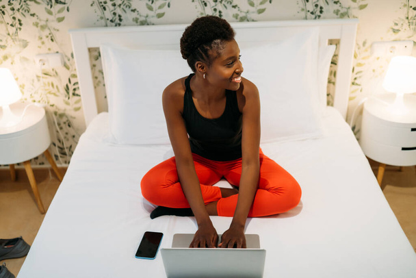 Attractive black woman using laptop on her bed at home - Photo, Image