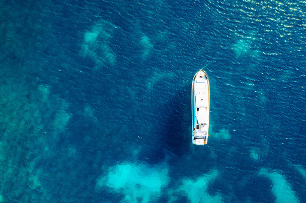 熱帯の島の前で透明なターコイズブルーの水の中でヨットの停泊,代替ライフスタイル,ボートに住んでいます.ターコイズブルーの水の上のアンカーでヨットの空中ビューは、豪華さ、富を示しています. - 写真・画像