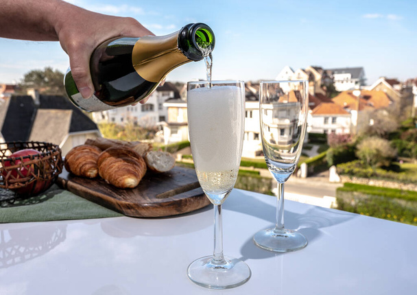 晴れた日にフランスの屋外テラスでフルートグラスにブリュットシャンパン輝くワインを注ぐ - 写真・画像