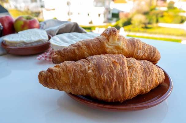 Frans ontbijt met vers gebakken croissants en kazen uit Normandië, camembert en neufchatel geserveerd buiten met mooi Frans dorpsuitzicht - Foto, afbeelding