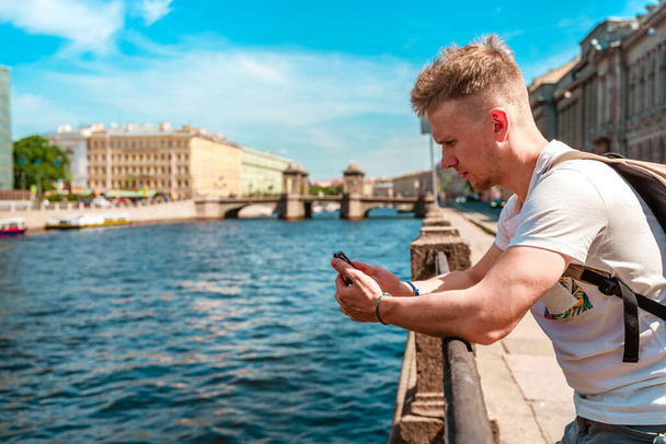 サンクトペテルブルクの堤防上の川の上に携帯電話を持っている若い男の手 - 写真・画像