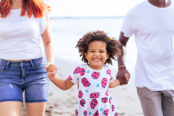 Hija caminando con sus padres a lo largo de la playa el día de verano. Verano, vacaciones y concepto familiar. - Foto, imagen
