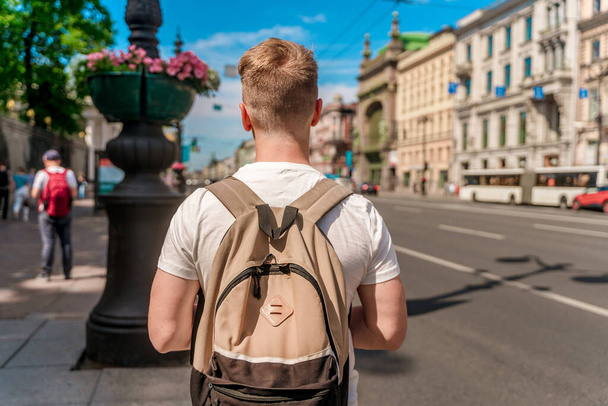 A young man with a blonde hair and a backpack walks in the center of the street in St. Petersburg in the summer - Foto, Imagem