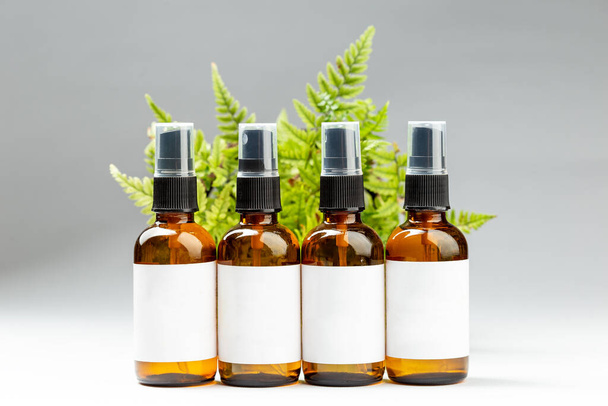 Set of dark amber glass spray bottles with white labels for cosmetic product over green leaves background. Sustainable lifestyle, beauty salon treatment concept, minimalism brand packaging mock up - Photo, Image