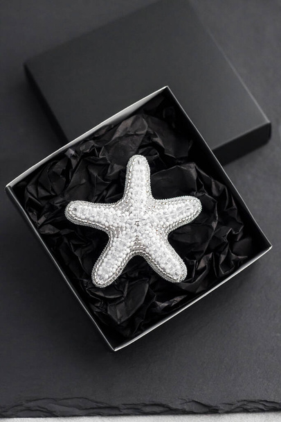 Seed bead embroidered brooch in a shape of starfish in black box on black background - Photo, Image