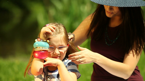 Молодая мать в соломенной шляпе расчесывает дочь на лугу или в парке
 - Кадры, видео