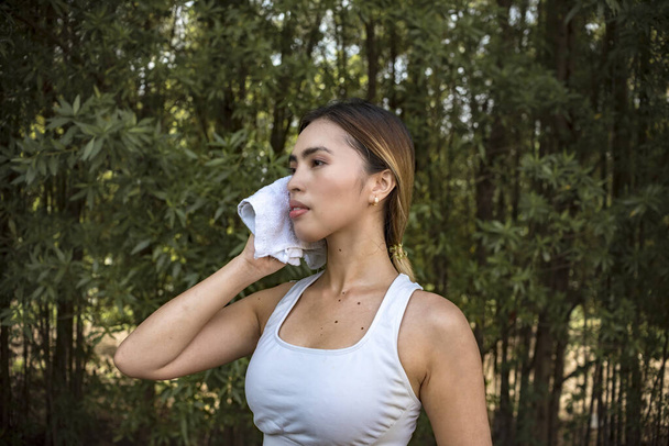 Une femme asiatique en forme et mince essuie la sueur avec une serviette pour le visage après un entraînement vigoureux à l'extérieur. Concept de mode de vie actif. - Photo, image