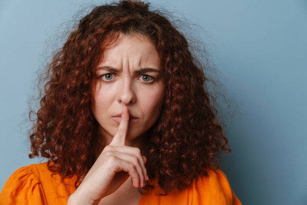 Displeased ginger young woman showing silence gesture isolated over blue background - Foto, Bild