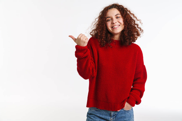 Joyful ginger curly girl smiling and pointing finger aside isolated over white background - Zdjęcie, obraz