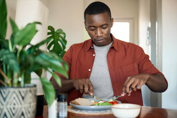 Young African man sitting at his dining room table enjoying a healthy home cooked egg breakfast - Foto, Imagem