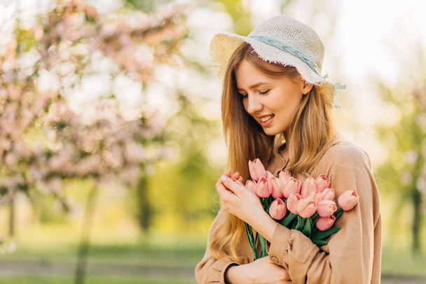 Happy beautiful young woman in a park with spring flowering trees, Beautiful spring blonde with pink flowers, against the background of a blooming park - Fotó, kép
