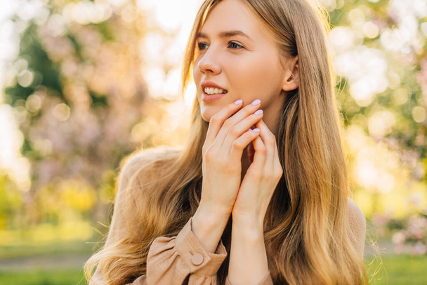 Portrait of a beautiful young woman smiling happily on a sunny summer or spring day outdoors in a park, in a dress, woman outdoors. - Foto, Bild