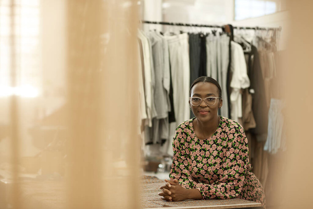 Portrait of a confident young African female fashion designer leaning on a workbench in her manufacturing studio - Foto, Imagen