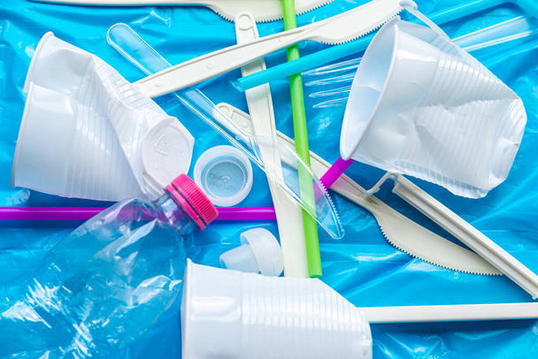 Residuos de plástico desechables, vasos, cuchillos, tenedores, botellas, en la superficie de plástico azul. Reciclaje y reutilización de plástico.  - Foto, imagen
