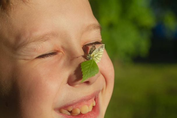 White butterfly on the nose on the face of a teenage boy, the child is smiling and happy. - Foto, immagini