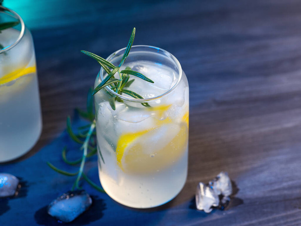 summer cold lemonade with lemon and rosemary in glasses. copy space wooden table - Photo, Image