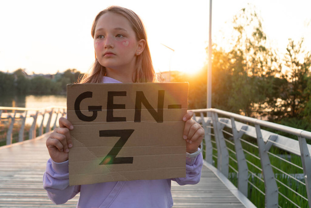 A stylish teenage girl in a purple hoodie with pink hair holds a sign with an inscription in her hands generation Z. GEN Z STYLE  TRENDS. - Photo, Image