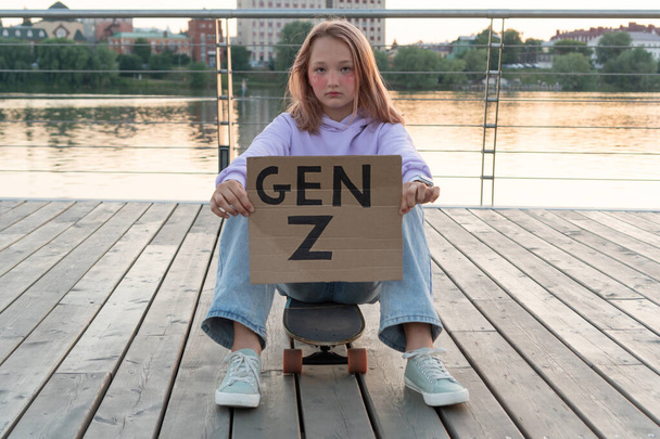 Stijlvol tienermeisje in een paarse hoodie en jeans met roze haar zit op een longboard en heeft een bordje met de inscriptie generatie Z. GEN Z STYLE TRENDS - Foto, afbeelding