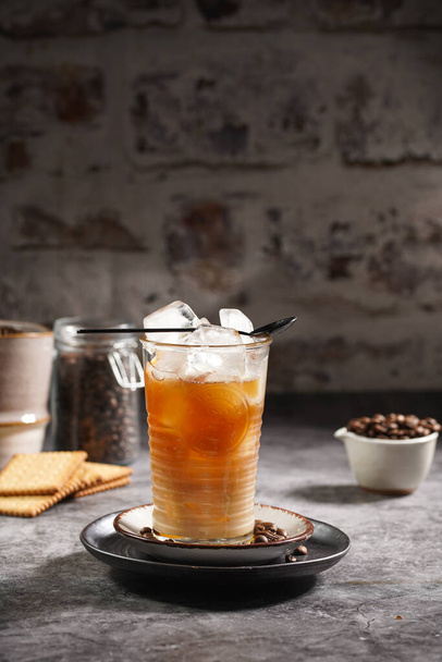 Ein schwarzer Teelöffel auf einem Glas mit Eiswürfeln und Kaffee - Foto, Bild