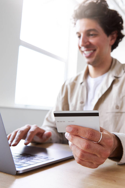 Alkalmanként öltözött fiatalember dolgozik az asztalnál laptop így online tranzakció hitelkártyával a modern nyílt terű irodában - Fotó, kép