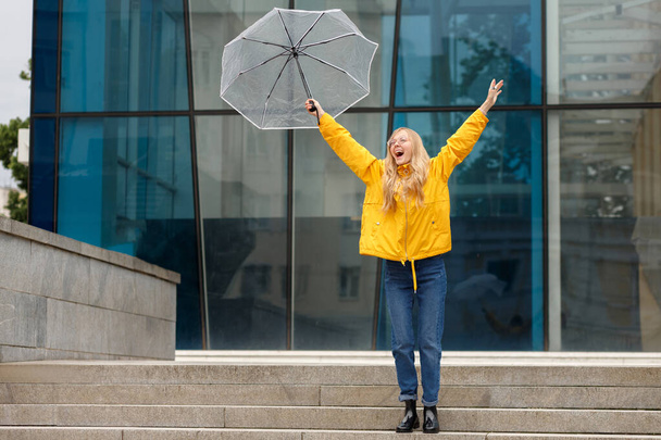 Şemsiyeli sarı yağmurluklu kız şehirde gülüp dans edecek. - Fotoğraf, Görsel