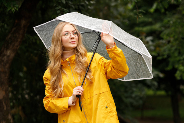 lány esőkabátban esernyővel ősszel a zöld háttér - Fotó, kép