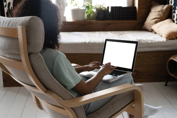 Mixed race Woman Working On Laptop Computer With Blank White Screen At Home, Sitting In Chair, Over Shoulder View - Photo, Image