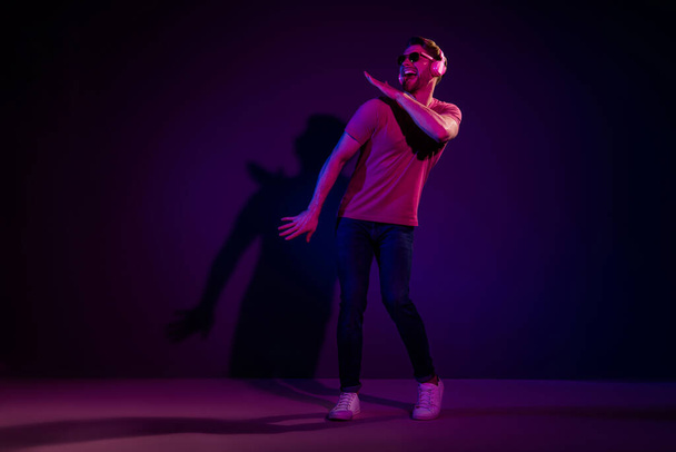 Full length body size view of attractive funny cheerful guy listening hit sound dancing isolated over dark neon violet color background - Foto, afbeelding