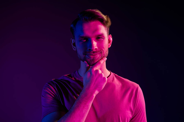 Portrait of attractive cheerful well-groomed guy touching chin isolated over dark neon light violet color background - Photo, Image