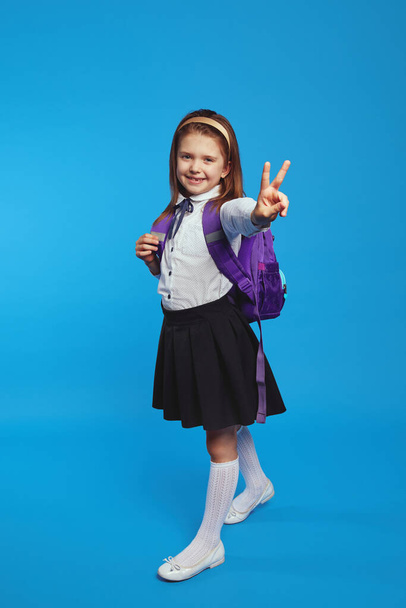 Studentessa indossa uniforme e zaino, sorridente e mostrando gesto di pace - Foto, immagini