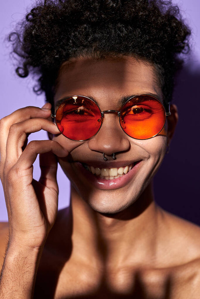 Vertikales Porträt eines Latino-Männchens in orangefarbener Brille aus nächster Nähe. Fröhliches Transgender-Modell perfekter Körper - Foto, Bild