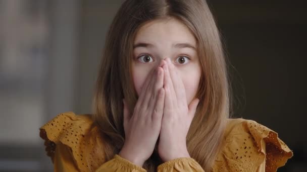 Portret kaukaski dziewczyna nastolatka uczennica dziecko córka młodsza siostra uczeń czuje szok otwiera usta z zaskoczeniem zdumienie cud obejmuje twarz z rąk patrząc na aparat pozowanie wewnątrz - Materiał filmowy, wideo