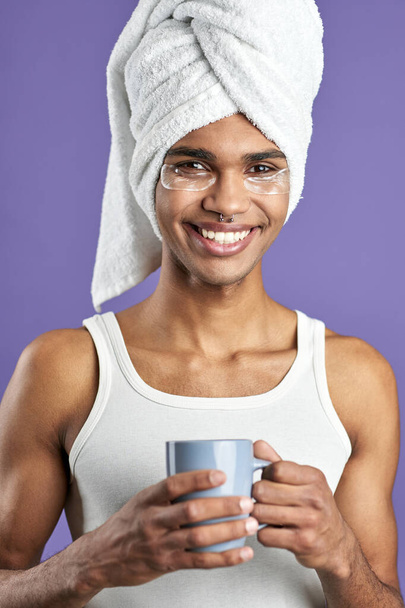 Молодой человек с повязками на глазу в полотенце на голове и чашке чая портрет - Фото, изображение