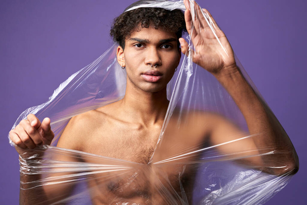 Junger Transgender-Mann mit zerstörter Plastiktüte am nackten muskulösen Körper. Transgender-Mann kann atmen - Foto, Bild