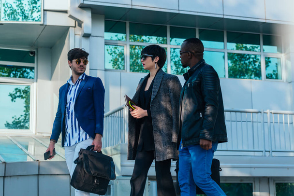 Groupe de trois collègues d'affaires multiethniques qui discutent en marchant dehors pendant une pause - Photo, image