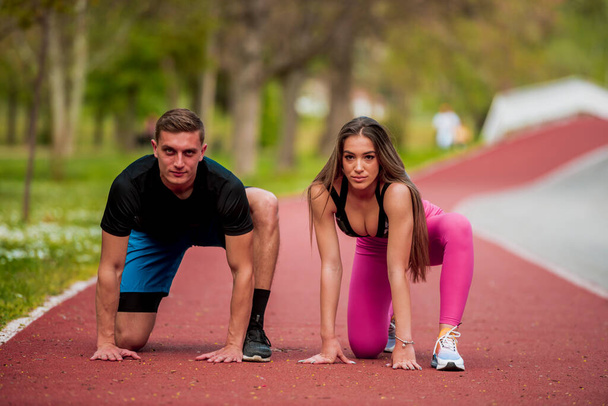 Attractive couple getting ready for the race in city park area. Training and exercising for endurance. Fitness healthy lifestyle concept outdoor - Foto, Imagem