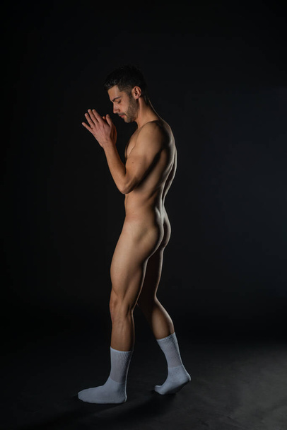 Full-length picture in a dark studio of a handsome naked man posing in white socks - Photo, Image