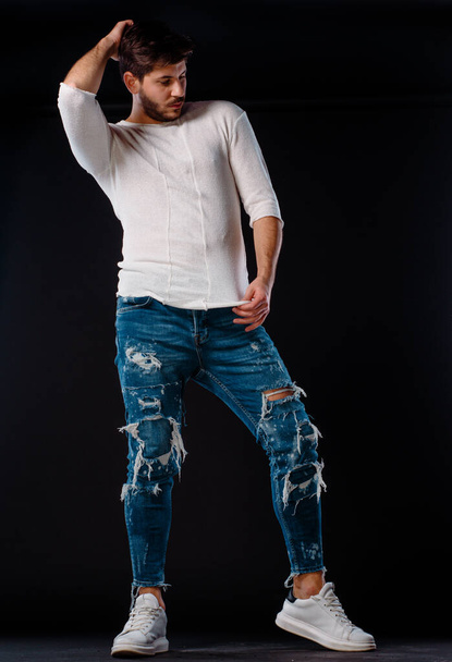 Jeune modèle masculin attrayant posant en jean bleu, haut blanc et chaussures de sport - Photo, image
