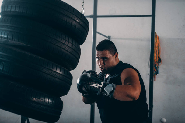 Boxer bonito no treinamento de luvas de boxe com pneus de perfuração no fundo escuro - Foto, Imagem