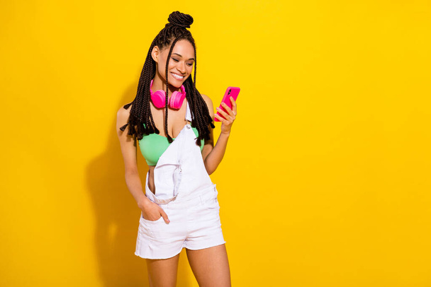 Photo of pretty charming dark skin lady wear green crop top headphones typing device empty space isolated yellow color background - Fotó, kép