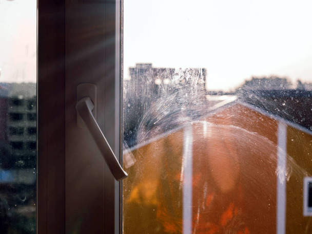 Schmutzige Fenster in der Wohnung vor dem Hintergrund des scharfen Morgenlichts. Schmutzige Flecken auf dem Glas. Reinigungskonzept, Fenster, das gewaschen werden muss - Foto, Bild